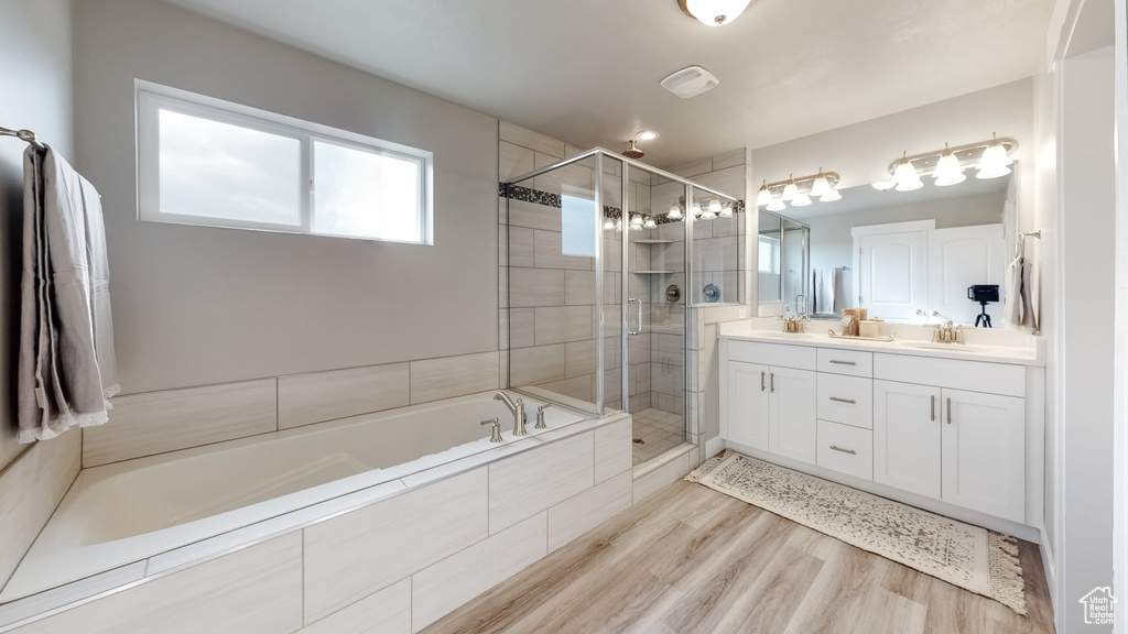 Bathroom featuring double vanity, a bath, a shower stall, and wood finished floors