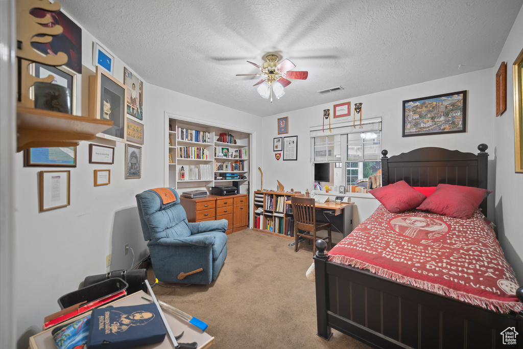 Carpeted bedroom featuring a textured ceiling, an office area, and a ceiling fan