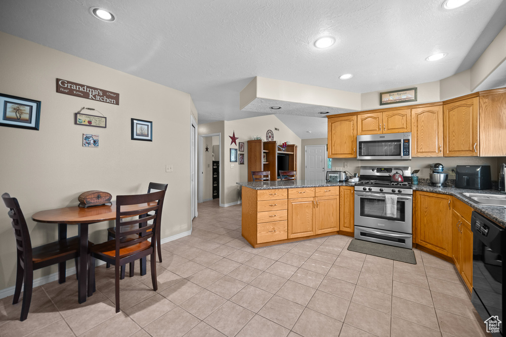 Kitchen featuring appliances with stainless steel finishes, a peninsula, light tile patterned flooring, a textured ceiling, and dark stone counters
