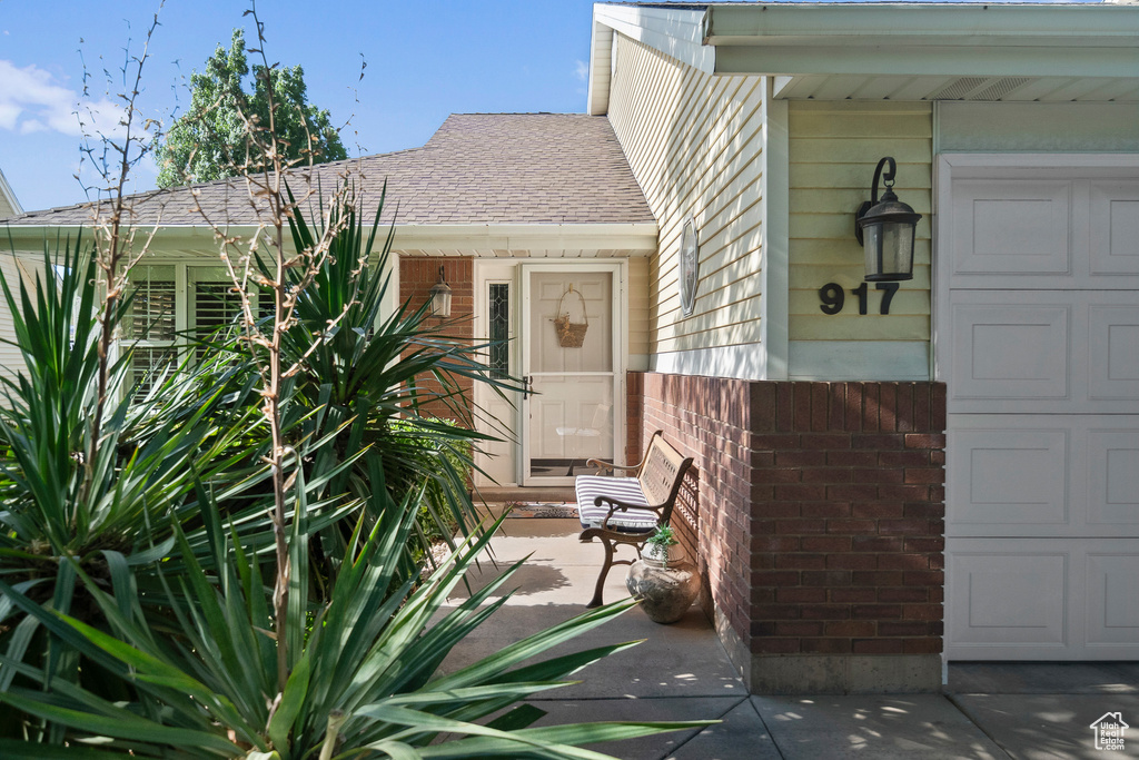 View of exterior entry with brick siding and a shingled roof