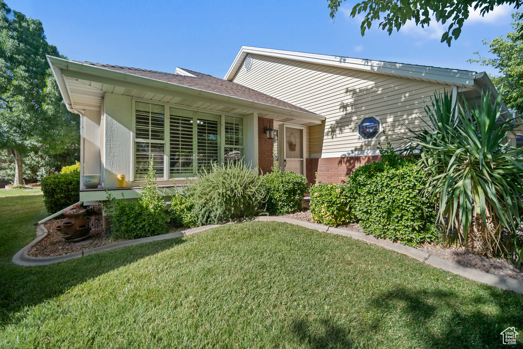 View of front facade with a front yard, brick siding, and roof with shingles
