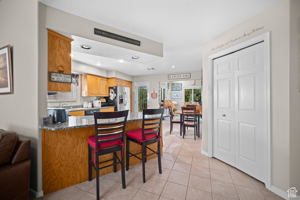 Kitchen with stainless steel fridge, a peninsula, light tile patterned flooring, a breakfast bar area, and recessed lighting