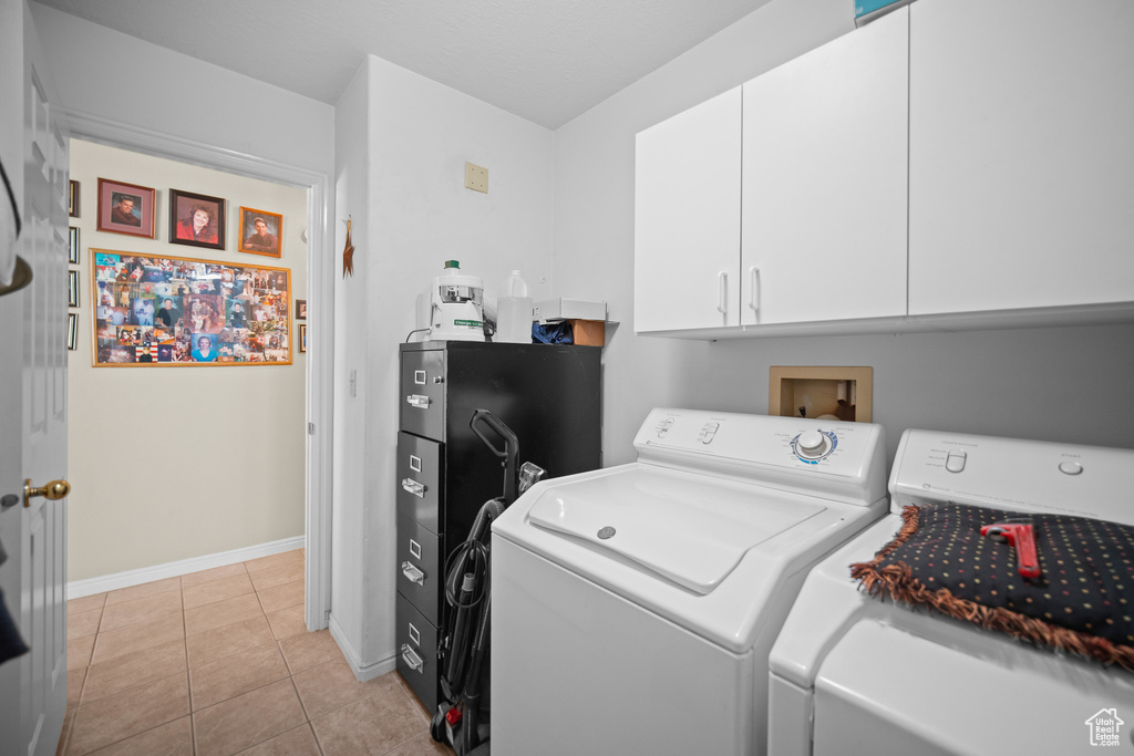 Washroom featuring washing machine and clothes dryer, cabinet space, and light tile patterned flooring
