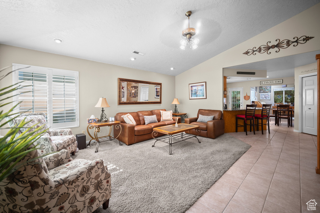 Living room featuring lofted ceiling, light tile patterned flooring, a ceiling fan, and a textured ceiling