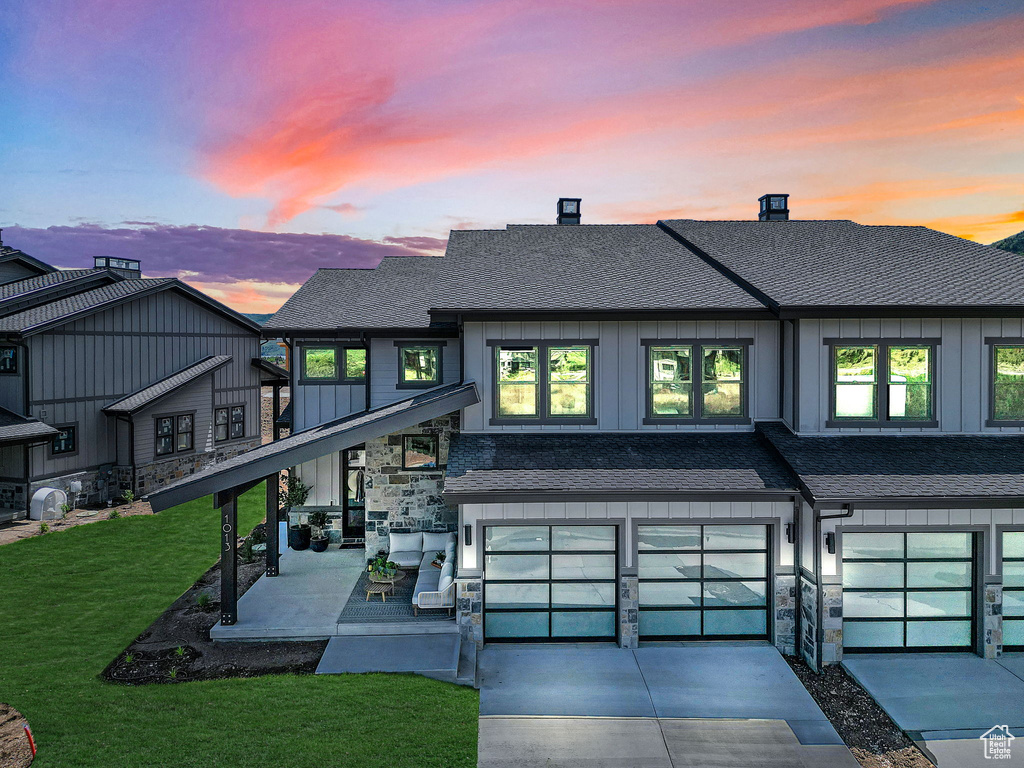 View of front facade featuring an attached garage, a shingled roof, concrete driveway, stone siding, and board and batten siding