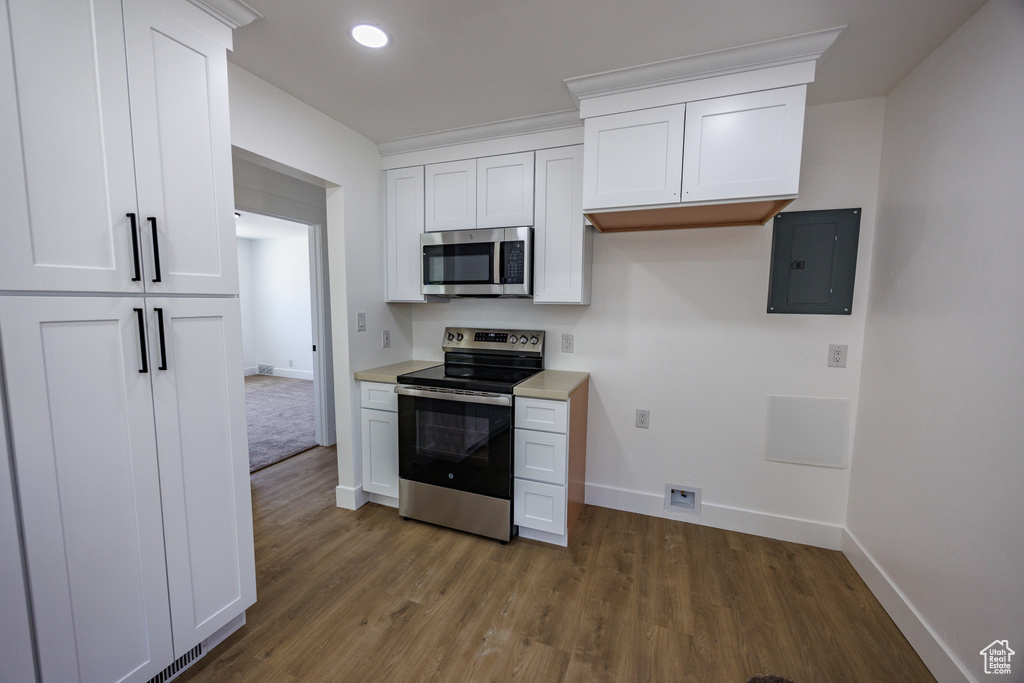 Kitchen with stainless steel appliances, electric panel, wood finished floors, white cabinetry, and recessed lighting