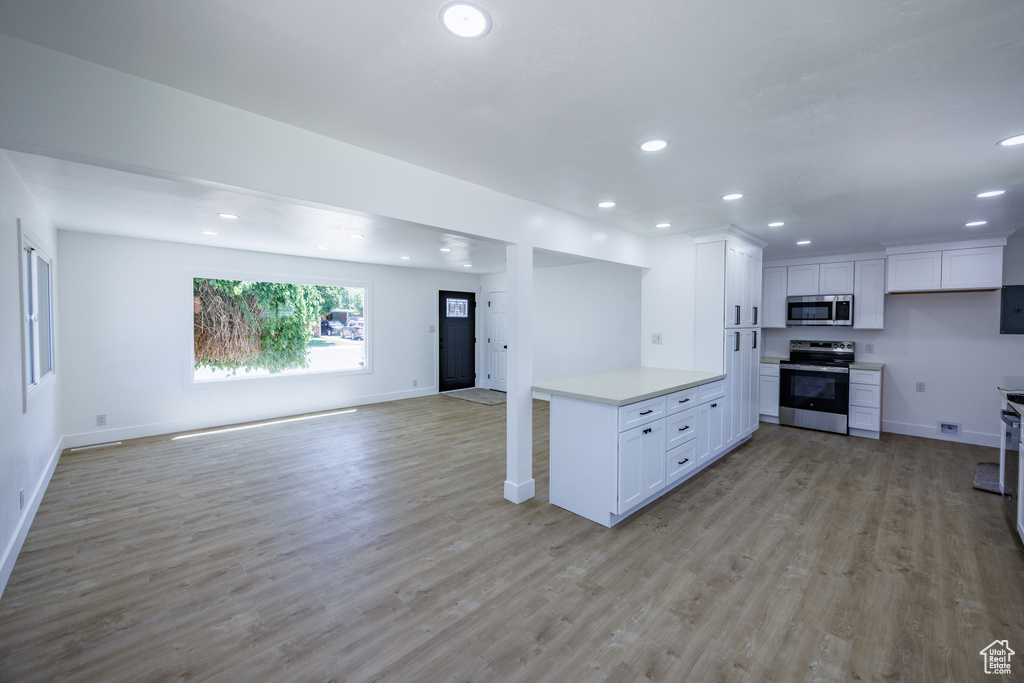 Kitchen with appliances with stainless steel finishes, open floor plan, recessed lighting, light countertops, and light wood-type flooring