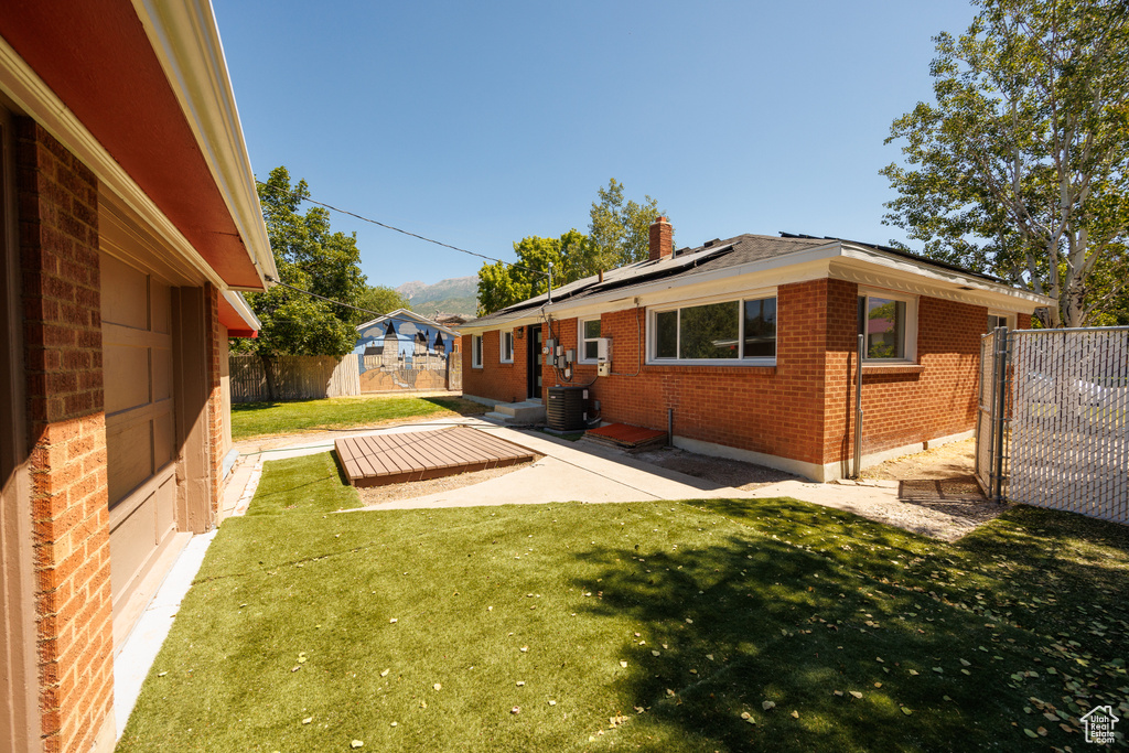 Rear view of property featuring brick siding, roof mounted solar panels, a fenced backyard, a patio, and a chimney