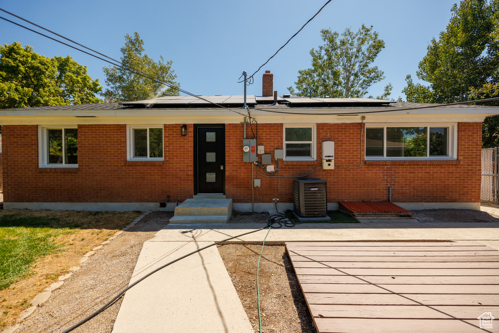 View of front of property with brick siding, roof mounted solar panels, a chimney, and entry steps