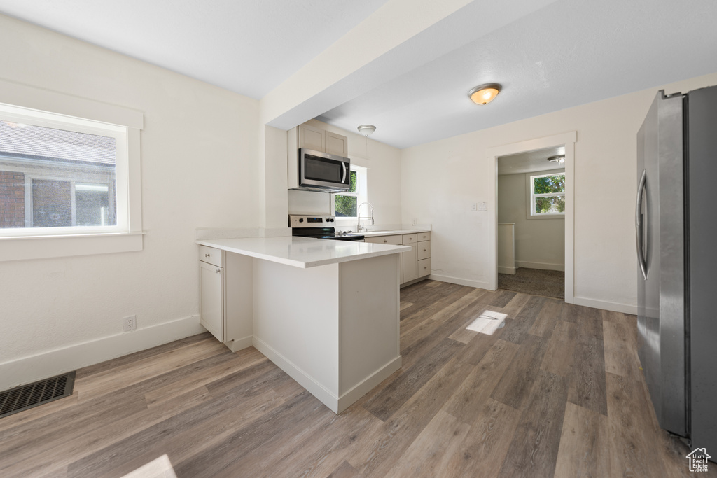 Kitchen with stainless steel appliances, a peninsula, light countertops, and light wood-style flooring