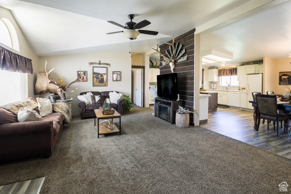 Carpeted living area with a ceiling fan, vaulted ceiling, and wood finished floors