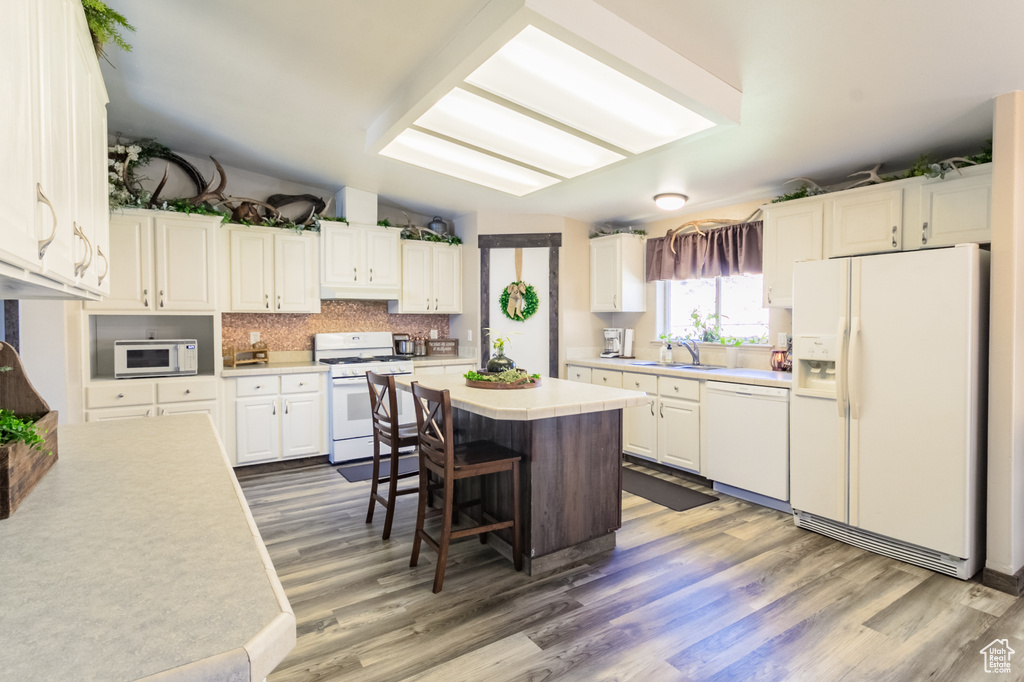 Kitchen with white appliances, wood finished floors, a kitchen bar, and light countertops