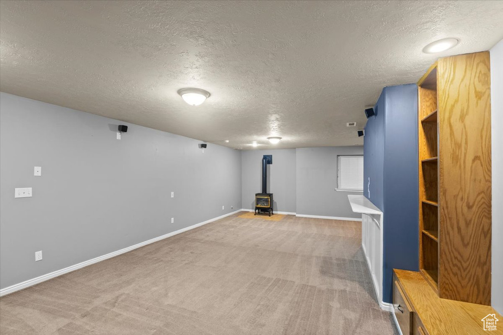 Finished basement with a wood stove, a textured ceiling, and light colored carpet