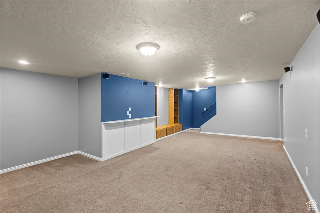 Finished basement featuring a textured ceiling, carpet flooring, and built in shelves