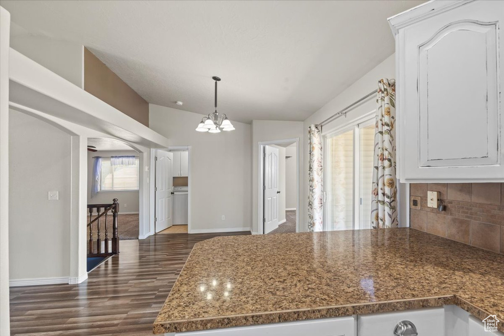 Kitchen with a chandelier, tasteful backsplash, dark wood-style flooring, white cabinets, and a peninsula