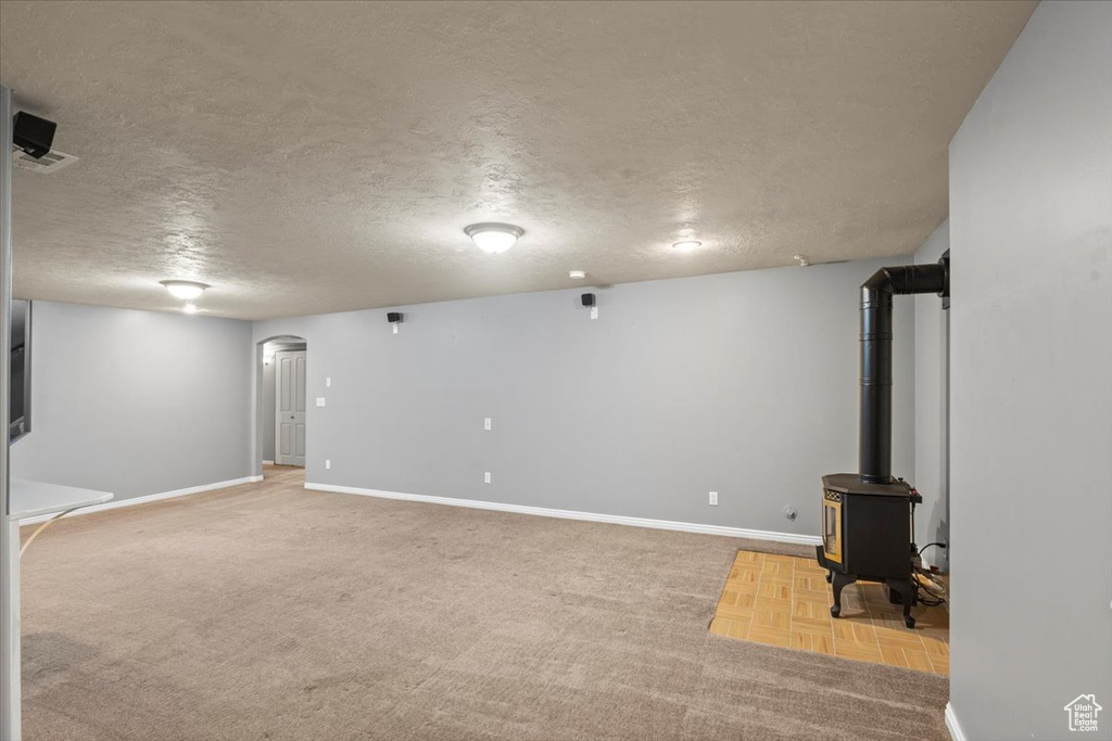 Below grade area featuring arched walkways, a textured ceiling, a wood stove, and carpet floors