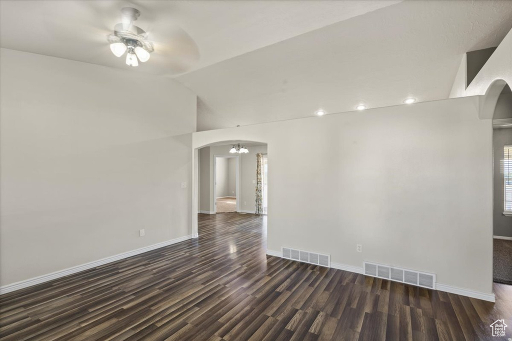 Empty room featuring arched walkways, ceiling fan, dark wood-type flooring, and vaulted ceiling