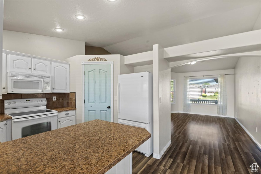Kitchen with white appliances, white cabinets, dark countertops, dark wood finished floors, and vaulted ceiling