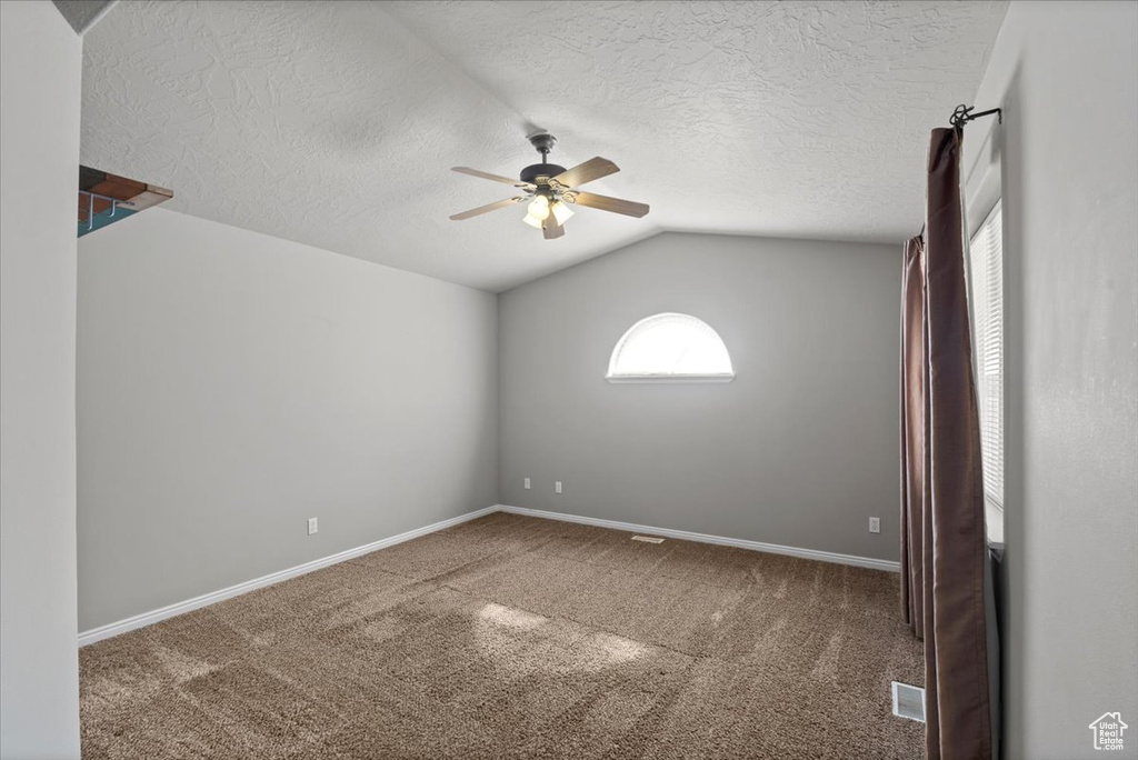 Carpeted empty room featuring ceiling fan, vaulted ceiling, and a textured ceiling