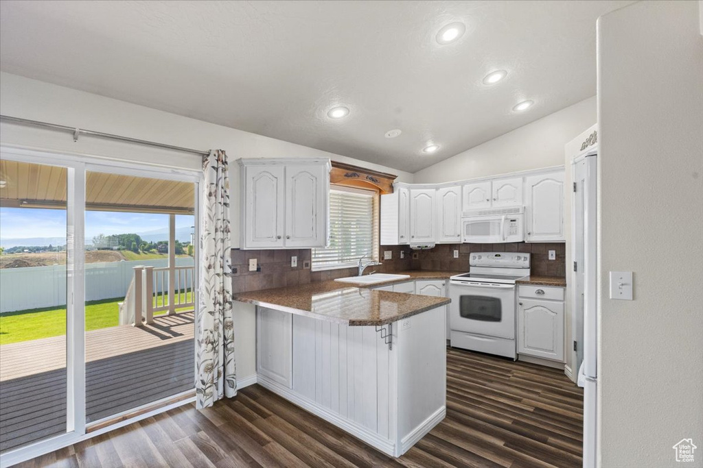 Kitchen featuring white appliances, a peninsula, white cabinets, dark wood-type flooring, and lofted ceiling