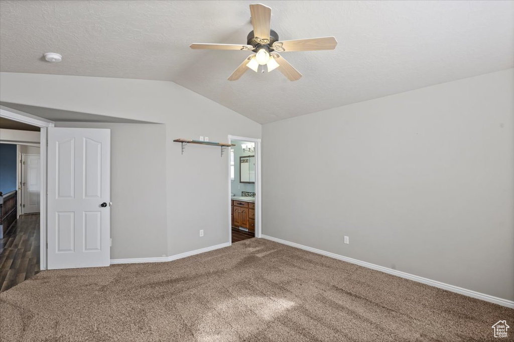 Unfurnished bedroom featuring carpet floors, vaulted ceiling, ensuite bath, a ceiling fan, and a textured ceiling