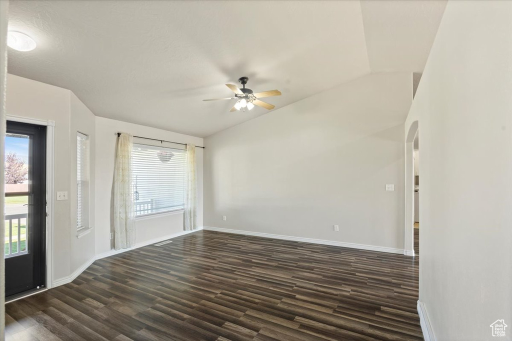 Empty room featuring a ceiling fan, healthy amount of natural light, dark wood-style flooring, and arched walkways
