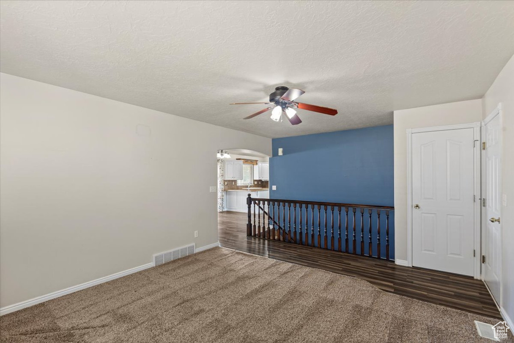 Carpeted spare room with a ceiling fan, arched walkways, and a textured ceiling