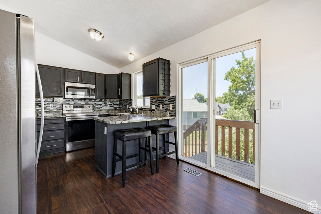 Kitchen with appliances with stainless steel finishes, backsplash, vaulted ceiling, a peninsula, and a breakfast bar area