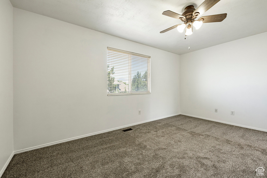 Carpeted spare room featuring a ceiling fan and baseboards