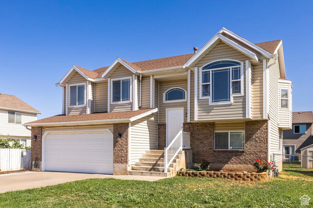 Raised ranch featuring a garage, concrete driveway, brick siding, and a shingled roof