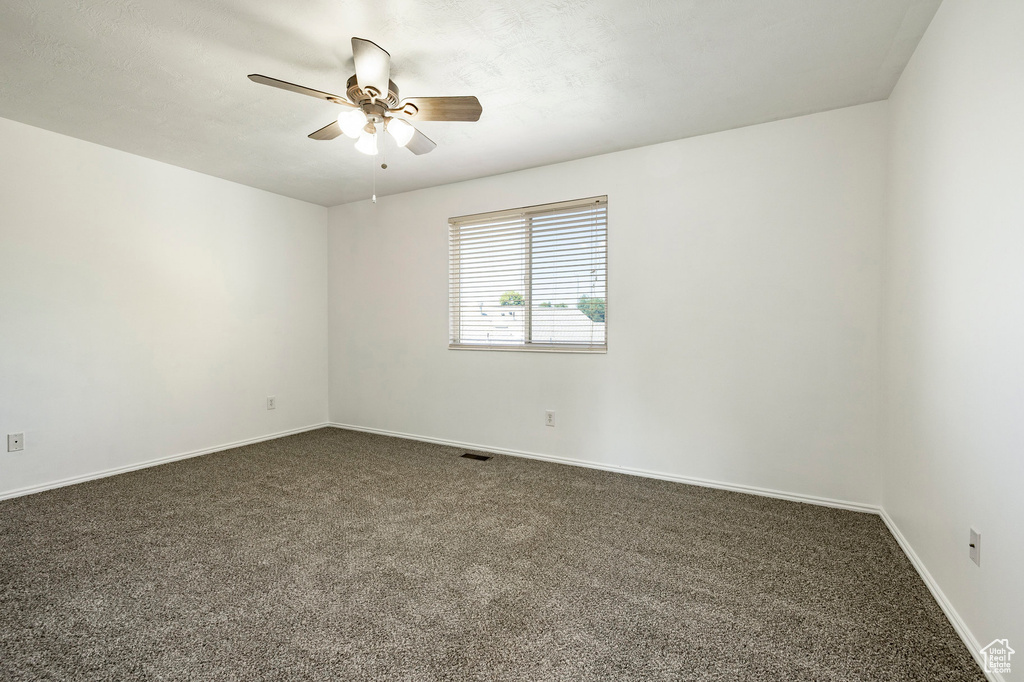 Empty room featuring dark carpet and a ceiling fan