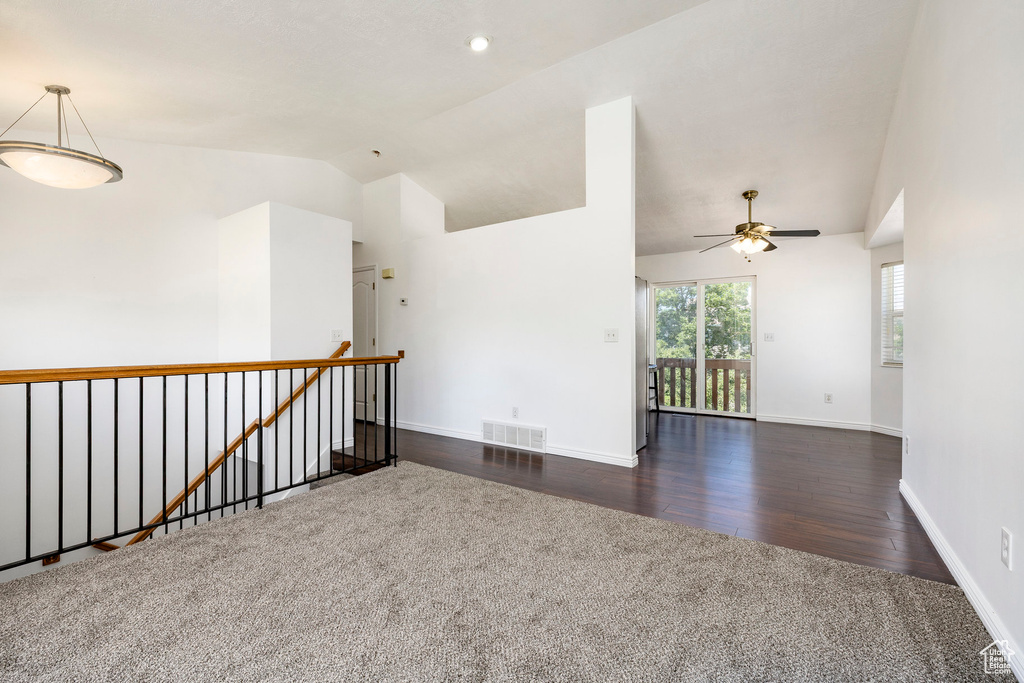 Carpeted empty room featuring ceiling fan, wood finished floors, and high vaulted ceiling
