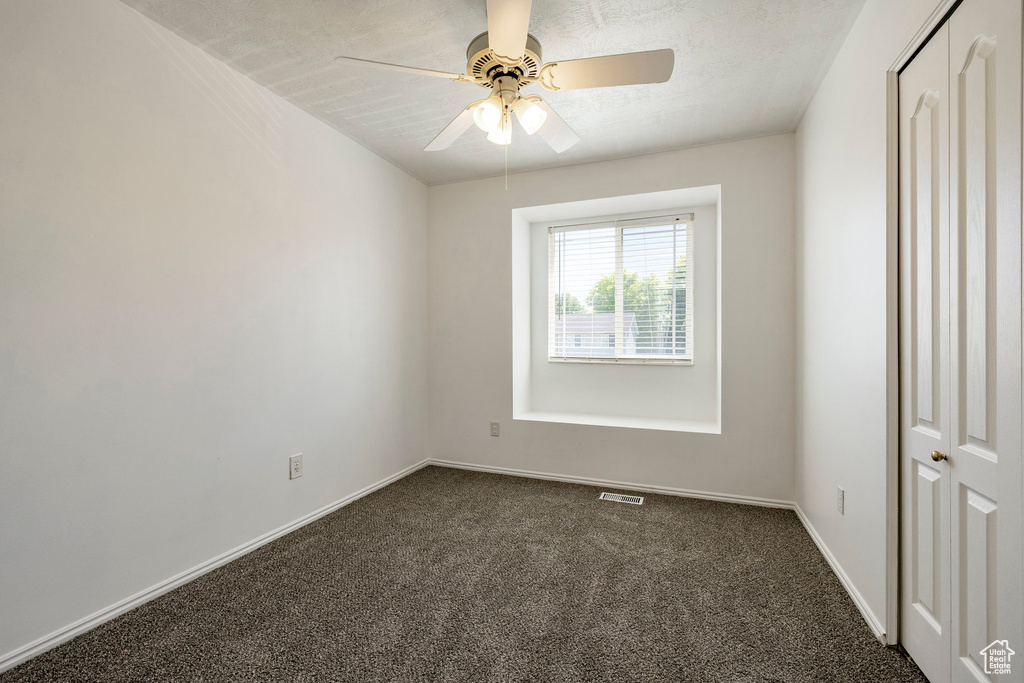 Empty room with dark carpet and a ceiling fan