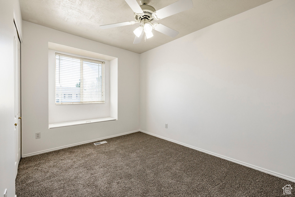 Spare room featuring dark carpet and ceiling fan