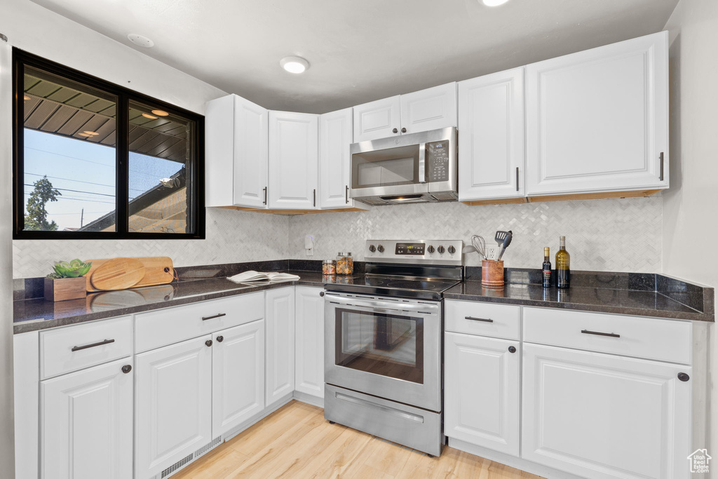 Kitchen with stainless steel appliances, light wood finished floors, white cabinetry, and dark stone counters