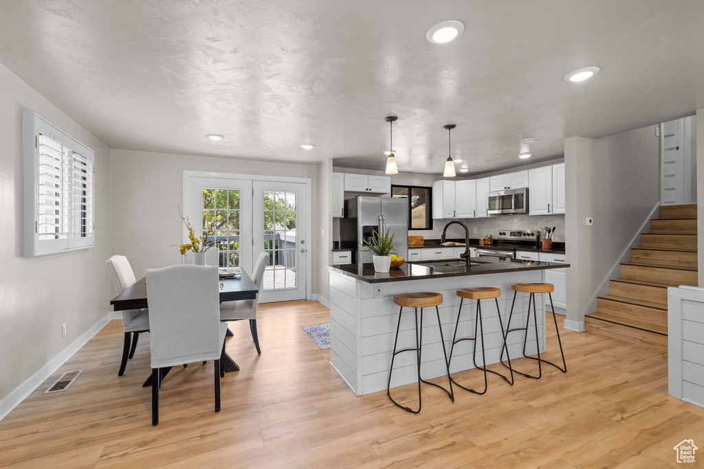 Kitchen featuring stainless steel appliances, dark countertops, white cabinetry, a kitchen breakfast bar, and recessed lighting