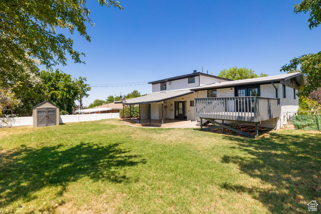 Back of house with a deck, a fenced backyard, a shed, brick siding, and a patio area