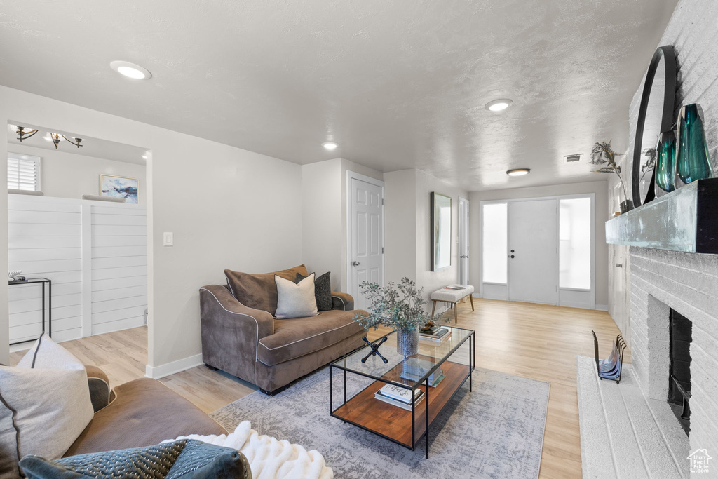 Living room with a fireplace, light wood-type flooring, a chandelier, and recessed lighting