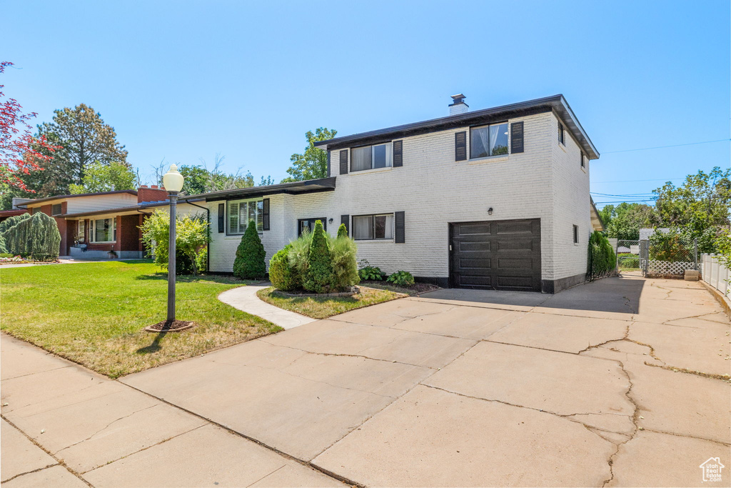 Tri-level home with brick siding, concrete driveway, a garage, and a chimney