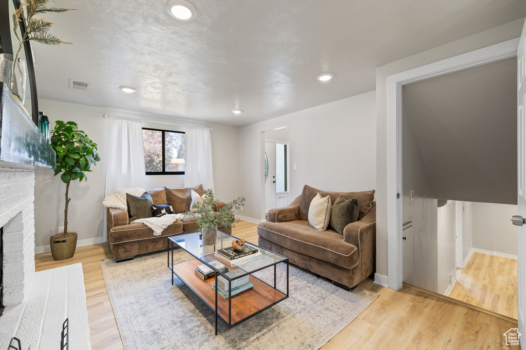 Living room featuring a brick fireplace, light wood-style flooring, and recessed lighting
