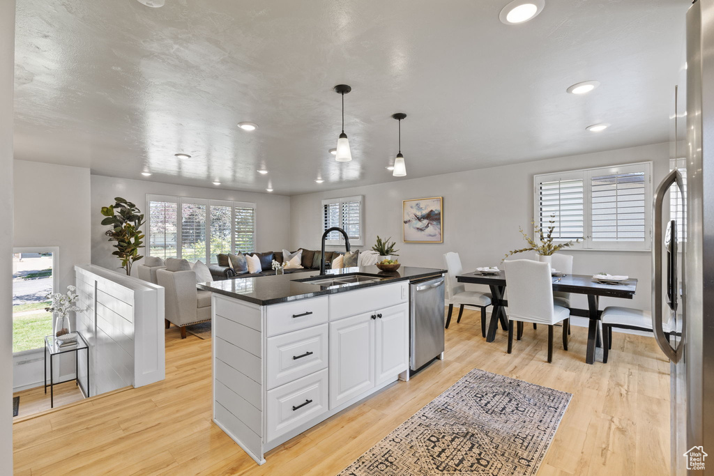 Kitchen with stainless steel appliances, dark countertops, white cabinets, light wood-style flooring, and recessed lighting