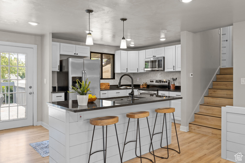 Kitchen with appliances with stainless steel finishes, a breakfast bar, backsplash, white cabinetry, and light wood finished floors