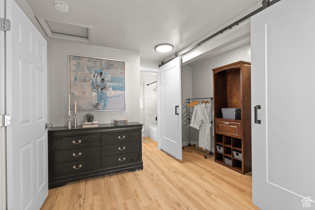 Bedroom featuring a barn door, light wood-style flooring, attic access, and ensuite bath