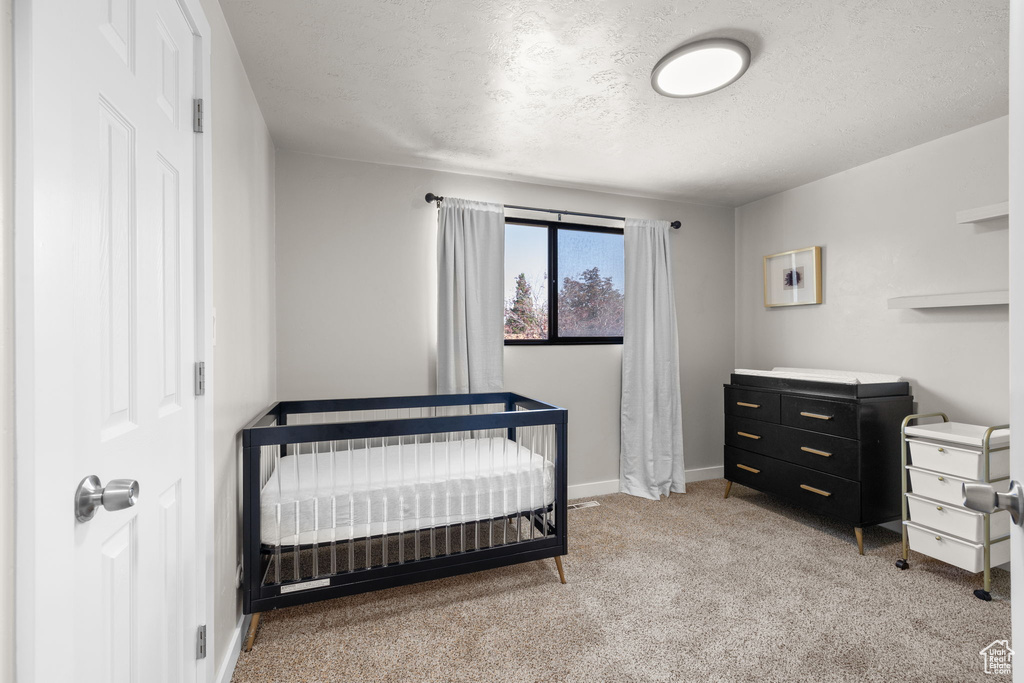 Bedroom with light colored carpet, a textured ceiling, and a crib