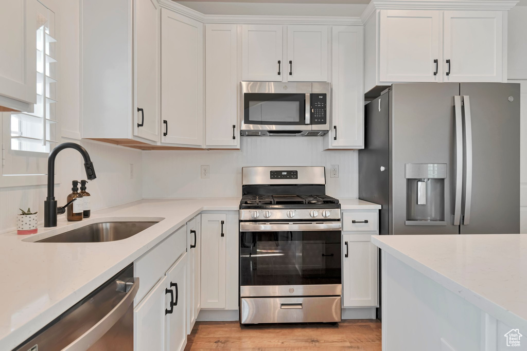 Kitchen with stainless steel appliances, white cabinetry, light wood-type flooring, and light stone countertops