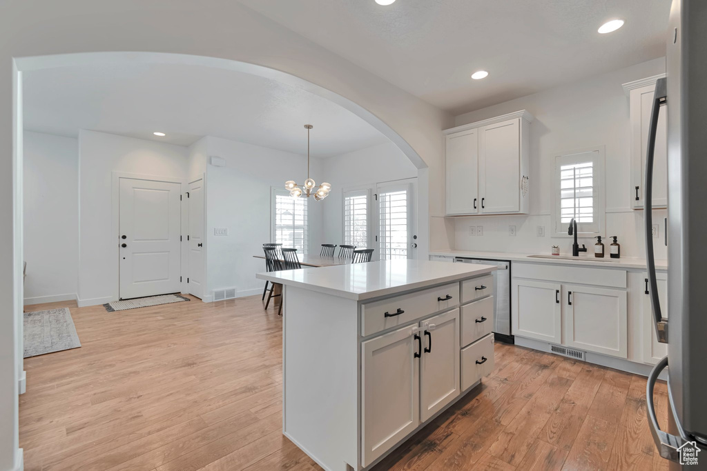 Kitchen with arched walkways, a chandelier, light wood-style floors, recessed lighting, and white cabinetry