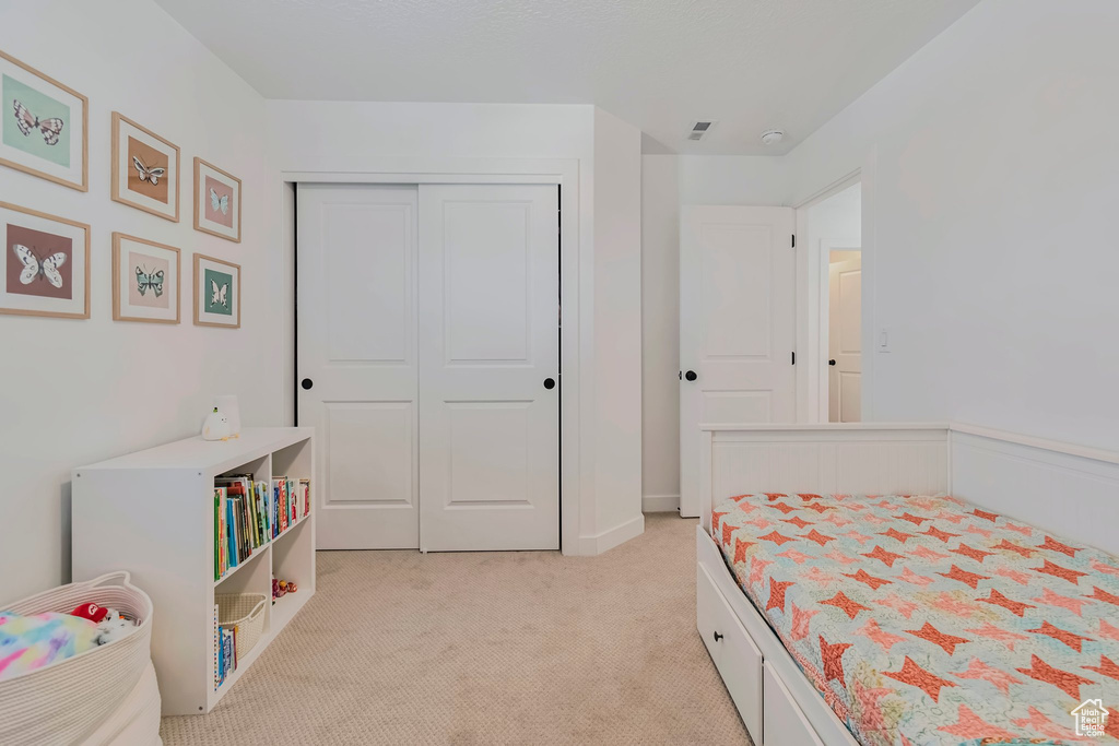 Bedroom with light colored carpet and a closet