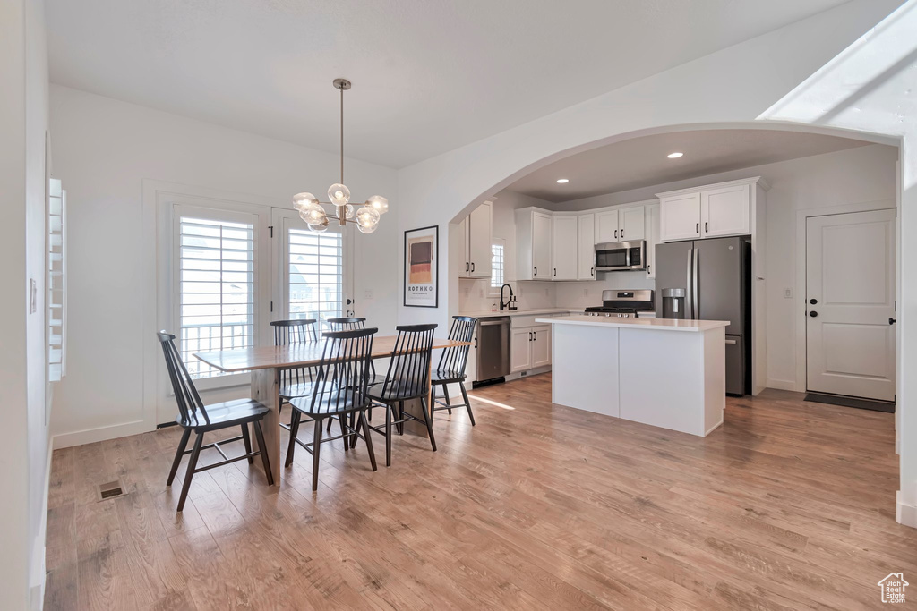 Dining space with a chandelier, light wood finished floors, arched walkways, and recessed lighting