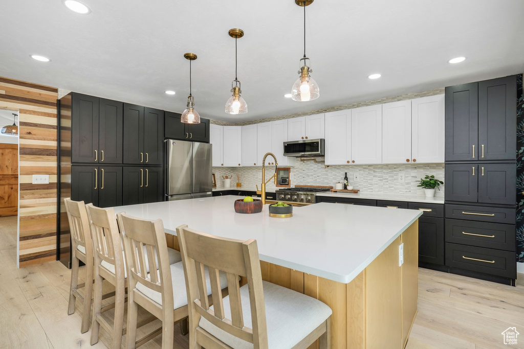 Kitchen with appliances with stainless steel finishes, light wood-style floors, recessed lighting, backsplash, and a breakfast bar area