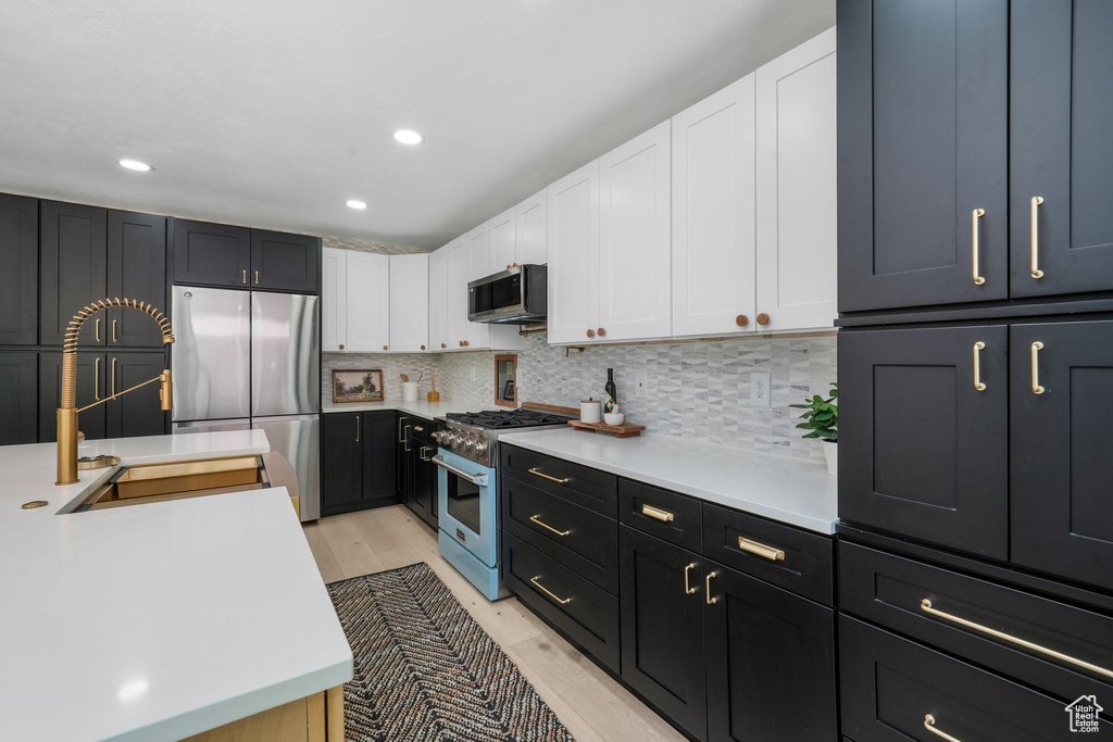 Kitchen with stainless steel appliances, white cabinets, light countertops, tasteful backsplash, and light wood-style flooring